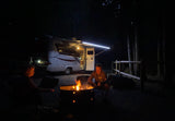 Nighttime camping by an RV rental. Two people relax by the fire pit's glow, ready for s'mores.