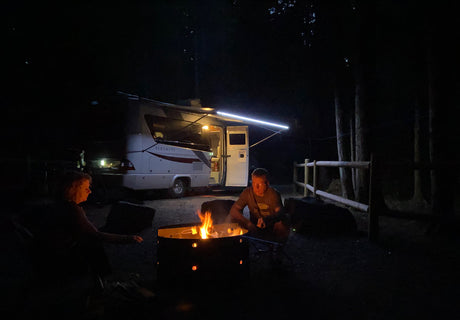 Nighttime camping by an RV rental. Two people relax by the fire pit's glow, ready for s'mores.