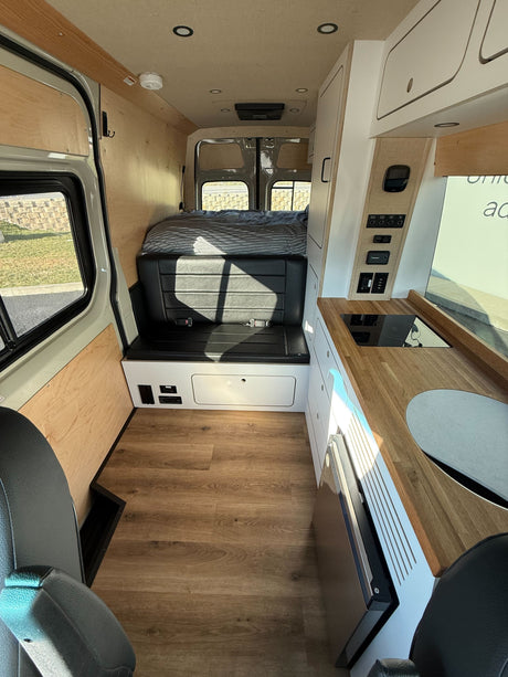 Modern camper van interior for rv rental, showing kitchenette, bed, and seating with wood floors.