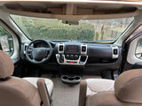 Interior of a modern RV rental, featuring the driver's cockpit with steering wheel, dashboard, and light-colored seats.