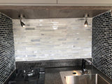 Modern RV rental kitchen featuring black/white tile backsplash, dark countertop, stainless sink, gas cooktop, and under-cabinet lighting.