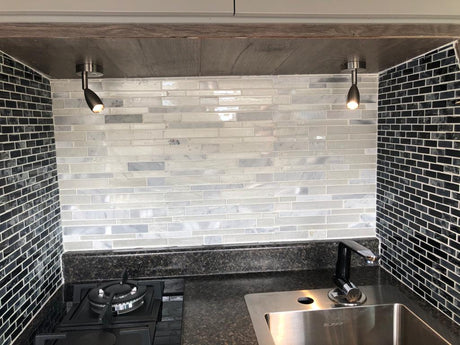 Modern RV rental kitchen featuring black/white tile backsplash, dark countertop, stainless sink, gas cooktop, and under-cabinet lighting.
