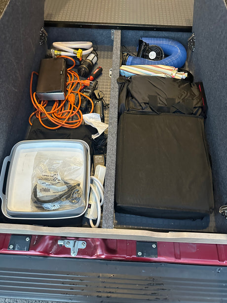 RV rental's rear storage, meticulously organized with hoses, power cords, fan, and essential camping gear.
