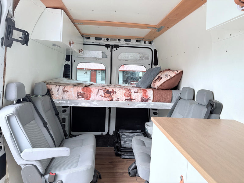 Explore this RV rental van conversion featuring a comfortable bed, passenger seats, storage cabinets, and wooden accents. — photo 5
