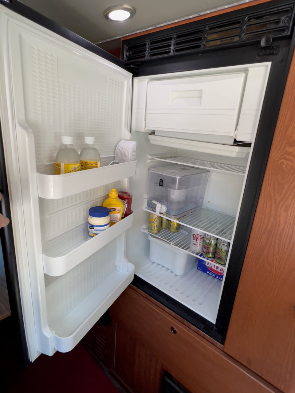 Open RV rental refrigerator showing drinks, condiments, and freezer. Stocked for your adventure!