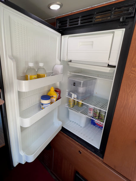 Open RV rental refrigerator showing drinks, condiments, and freezer. Stocked for your adventure!