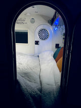 Cozy RV rental interior with a soft bed, "Adventure Awaits" decal, and colorful pillows.