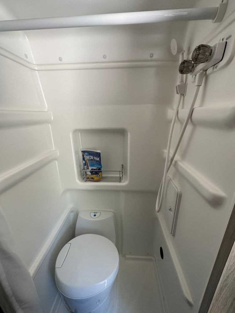 Compact RV rental wet bath featuring a toilet, handheld shower, and storage rack, maximizing space for travel convenience. — photo 13