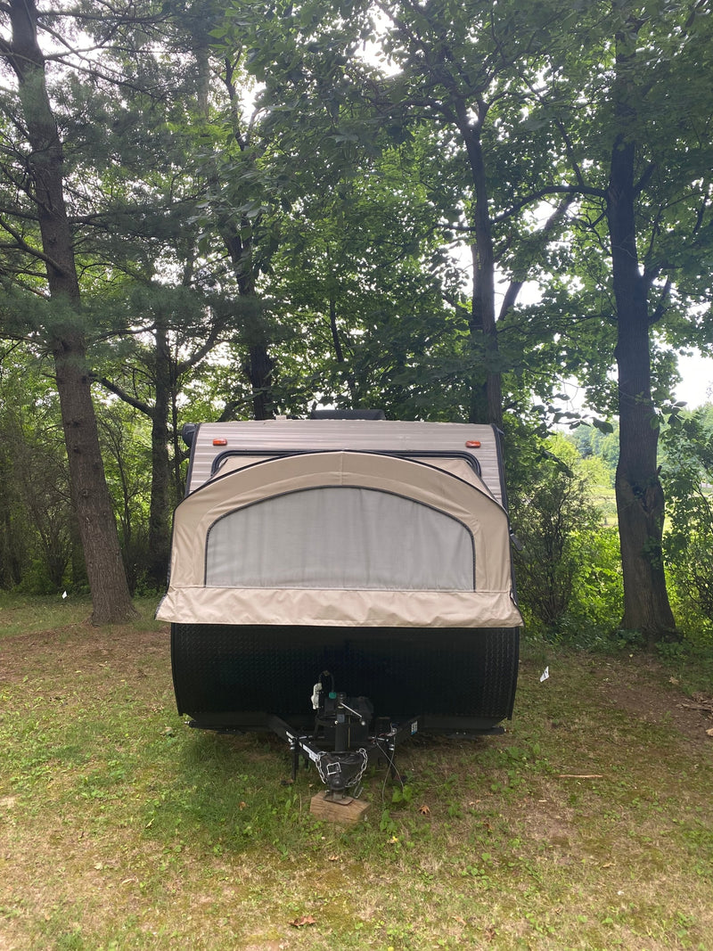 Front view of an RV rental: a beige pop-up camper parked on grass surrounded by lush green trees at a campsite. — photo 10