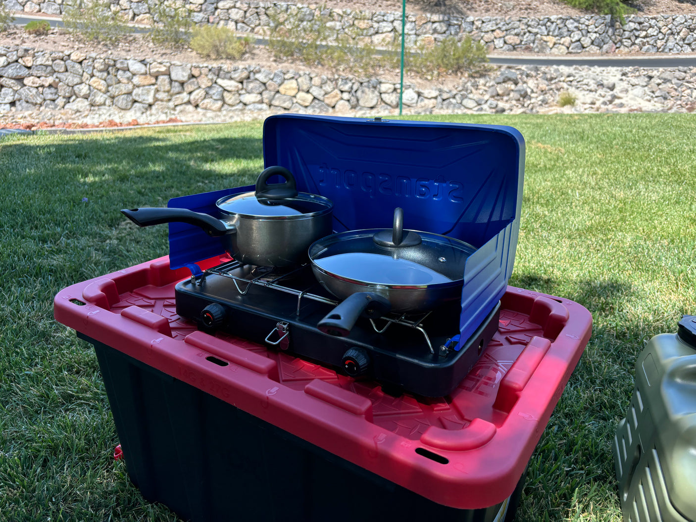 Enjoy your RV rental with this portable outdoor cooking setup: camp stove, pot, pan on a storage bin in the grass.