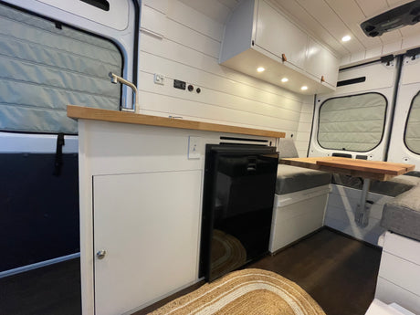 Bright, modern RV rental interior: a compact kitchen with a sink & fridge, and a cozy dinette space.