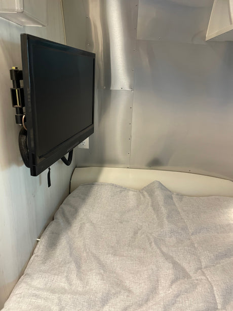 RV rental bedroom shows a wall-mounted black TV on aluminum walls, next to a bed with a light grey blanket.
