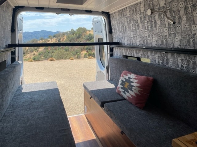 RV rental with comfy grey benches, owl wallpaper, and a metal bar. Enjoy mountain views from this camper van interior. — photo 5