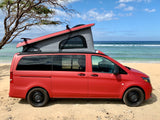 Red pop-top camper van RV rental parked on a sandy beach by the ocean. Ideal for a coastal adventure.