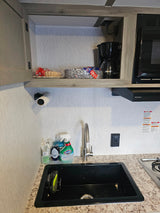 RV rental kitchen counter with a black sink, faucet, dish soap, coffee maker, microwave, and paper products.