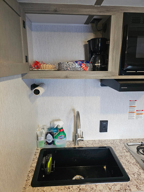 RV rental kitchen counter with a black sink, faucet, dish soap, coffee maker, microwave, and paper products.