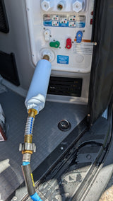 RV rental water hookup: A filter and blue hose connect to the utility panel for city water, with visible spills on the floor.