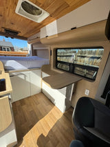 Modern RV rental interior: wood-paneled ceiling, comfy bed, sleek cabinetry, and a functional table workspace.