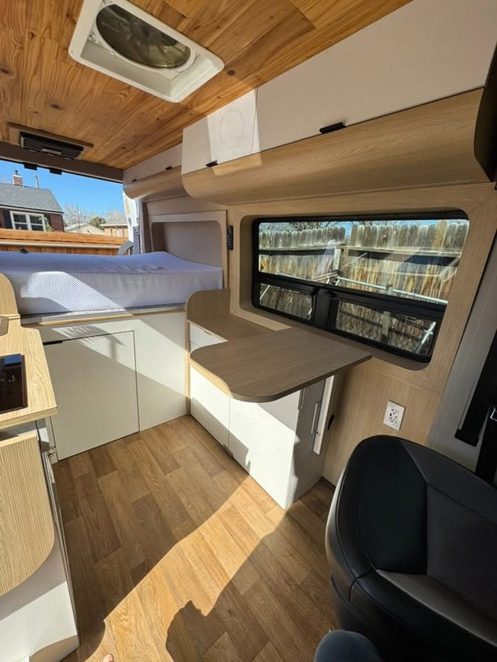 Modern RV rental interior: wood-paneled ceiling, comfy bed, sleek cabinetry, and a functional table workspace.
