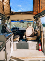 Experience freedom in this cozy RV rental camper van! Interior shows kitchen, seating, and pop-top with sky view.