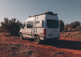 A white Storyteller Overland 4x4 RV rental van, a Mercedes Sprinter, parked on a red dirt trail.