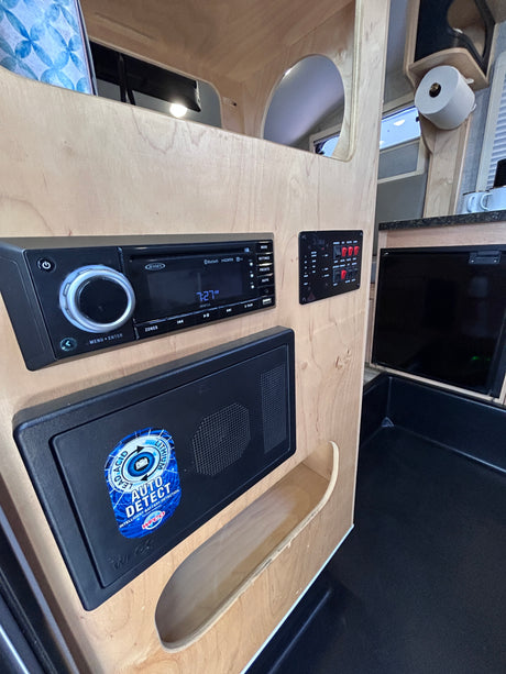 RV rental control hub: Jensen stereo, utility switches, and WFCO battery charger on wood, beside a dark sink.