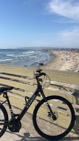 Black Trek bike on a pier overlooking a sunny, crowded beach. Perfect scenery for your next travel or rv rental adventure!