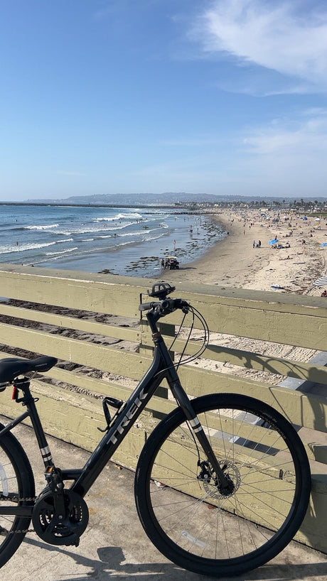 Black Trek bike on a pier overlooking a sunny, crowded beach. Perfect scenery for your next travel or rv rental adventure!