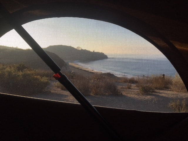  parked on a road beside a blue ocean and cliffs. Ideal RV rental scene.|RV rental window view: golden light illuminates a serene coastline with beach & ocean. A peaceful start to the day.|Compact RV rental interior: kitchen with stove & fridge — photo 2