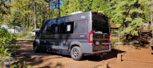 Dark gray camper van RV rental parked on a dirt road in a sunny forest campsite, perfect for outdoor travel. — photo 15