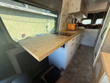 RV rental: Stylish camper van interior with a modern kitchenette, wood counter, induction cooktop, and bed area.