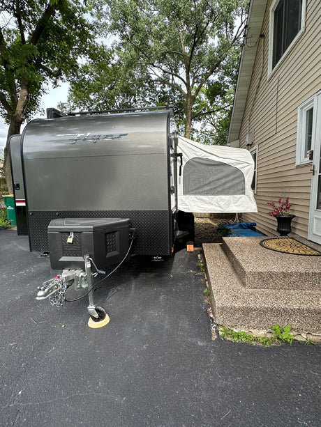 Grey Flyer travel trailer, a compact pop-up camper for your next RV rental, parked beside a house. Ready for adventure.