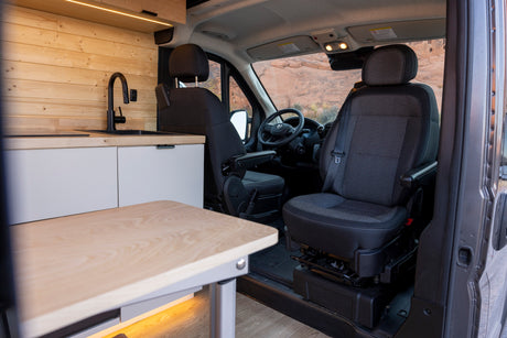 Spacious RV rental interior featuring a modern kitchenette, swivel seats, and a scenic view of rocky landscapes.