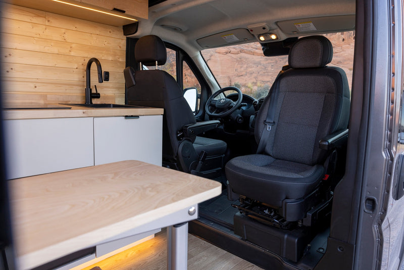 Spacious RV rental interior featuring a modern kitchenette, swivel seats, and a scenic view of rocky landscapes. — photo 8