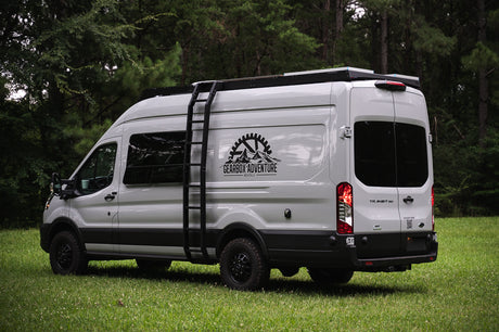 Explore with this white custom Ford Transit RV rental van from Gearbox Adventure Rentals, parked in a lush field.