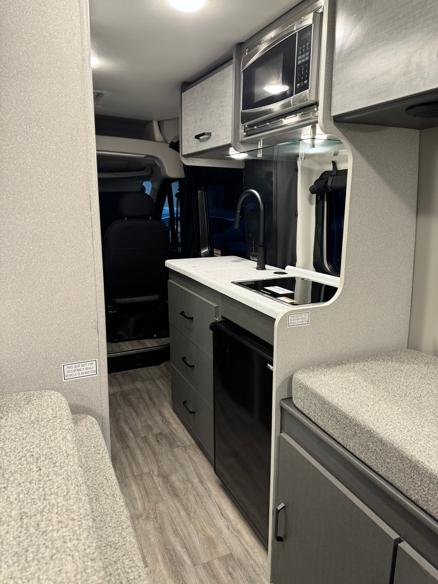 Compact RV rental interior featuring a functional kitchen with sink, microwave, fridge, and cozy seating. Perfect for travel.