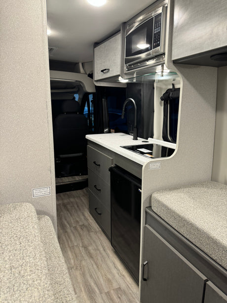 Compact RV rental interior featuring a functional kitchen with sink, microwave, fridge, and cozy seating. Perfect for travel.