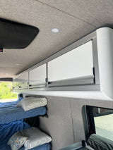 Inside a modern RV rental: bunk beds, bright overhead cabinets, and soft upholstered walls/ceiling.