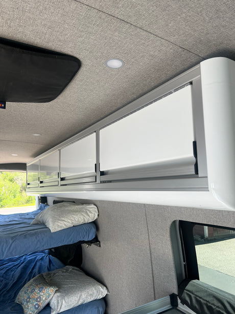 Inside a modern RV rental: bunk beds, bright overhead cabinets, and soft upholstered walls/ceiling.