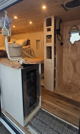 Stylish RV rental interior: wooden ceiling, live-edge counter, mini-fridge, bed, shower, and custom storage.