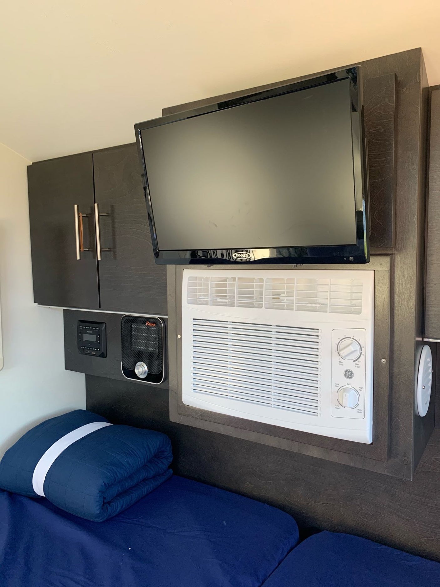 Compact RV rental interior featuring a TV, AC unit, heater, storage cabinets, and comfortable bed.