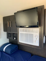 Compact RV rental interior featuring a TV, AC unit, heater, storage cabinets, and comfortable bed.