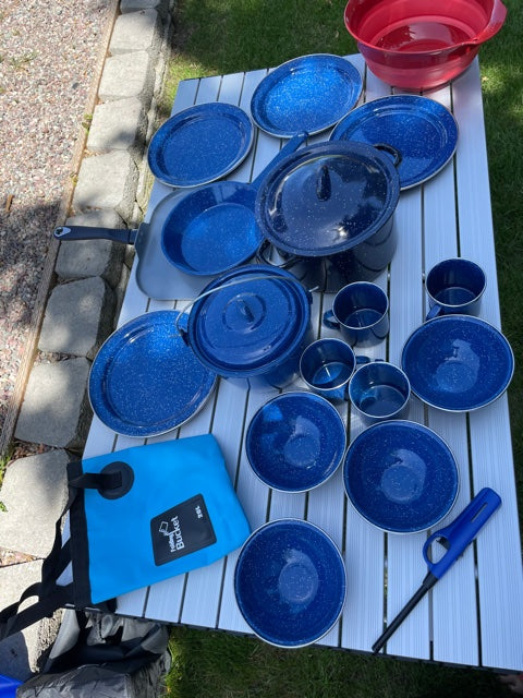 Essential RV rental camping kitchen: blue enamelware dishes, pots, pans, and a folding bucket on an outdoor table.