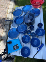Essential RV rental camping kitchen: blue enamelware dishes, pots, pans, and a folding bucket on an outdoor table.