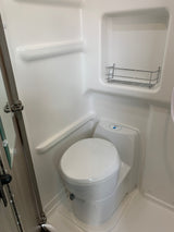 RV rental compact white shower/toilet combo. Features molded interior, chrome rack, and a Thetford chemical toilet.
