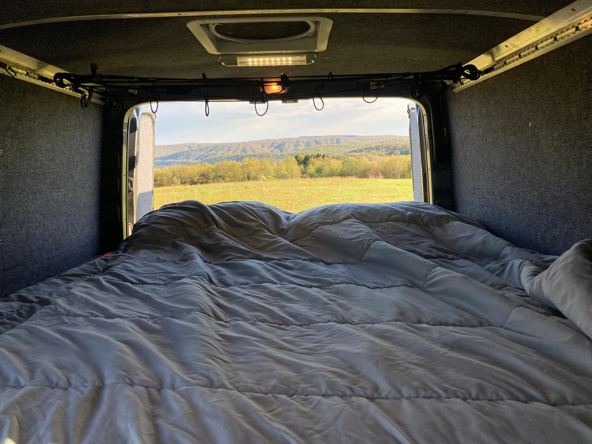 Cozy rv rental interior with a comfortable bed facing open back doors, revealing a scenic field and distant green mountains. — photo 12