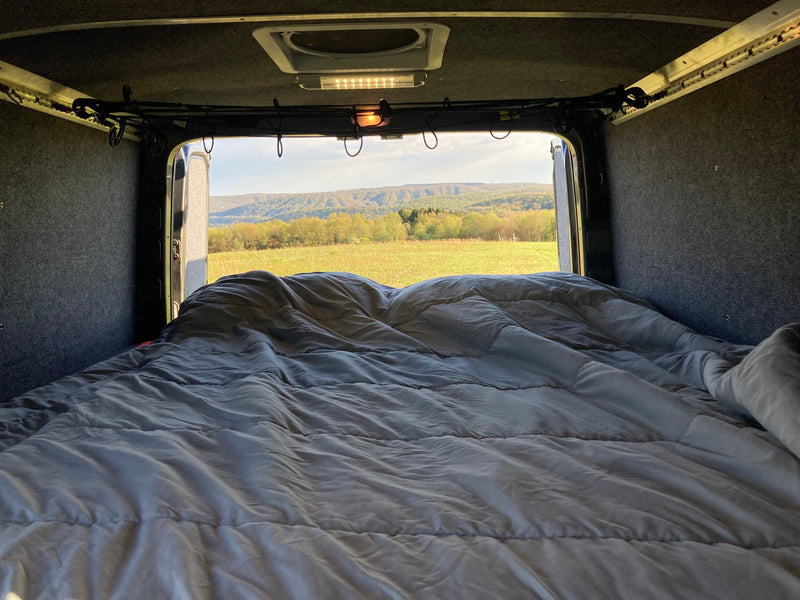 Cozy rv rental interior with a comfortable bed facing open back doors, revealing a scenic field and distant green mountains. — photo 12