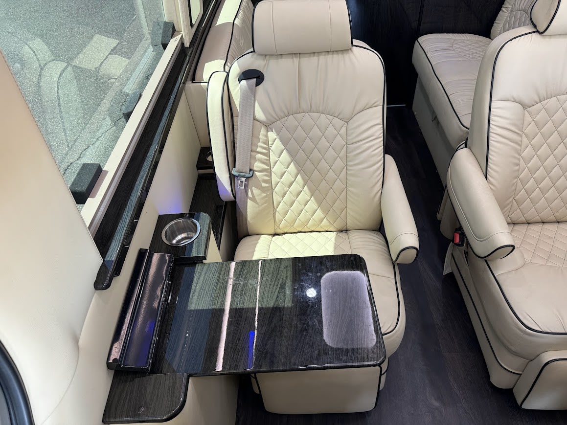 Comfortable RV rental interior showing cream quilted leather captain's chairs, a fold-out table, and a cup holder. — photo 10