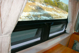 RV rental window with screens and white curtains, offering a view of a snowy hillside.