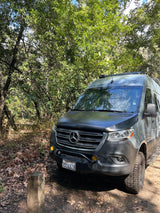 Adventure-ready Mercedes Sprinter van, perfect for an RV rental, parked on a dirt path in a sunny forest.
